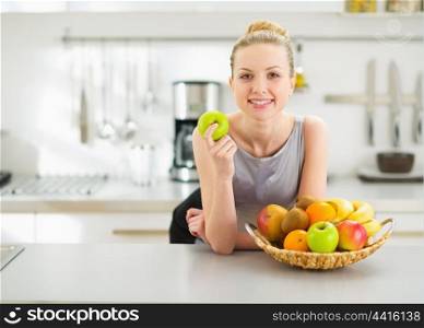 Happy young housewife with apple in modern kitchen