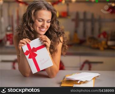 Happy young housewife with christmas postcard in kitchen