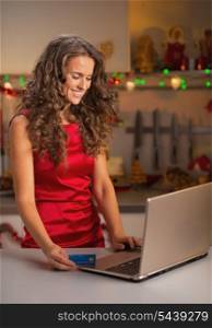 Happy young housewife with credit card usign laptop
