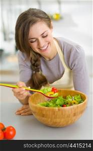 Happy young housewife with fresh vegetable salad in kitchen