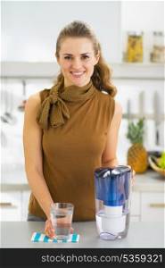 Happy young housewife with glass of water and water filter pitcher