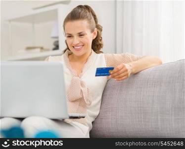 Happy young housewife with laptop and credit card in living room