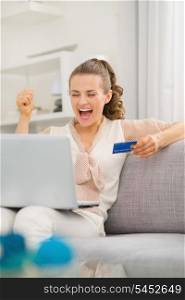 Happy young housewife with laptop and credit card rejoicing success