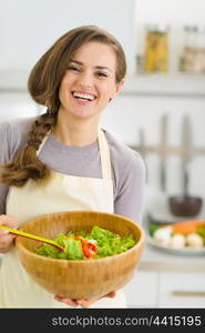 Happy young housewife with plate of fresh vegetable salad