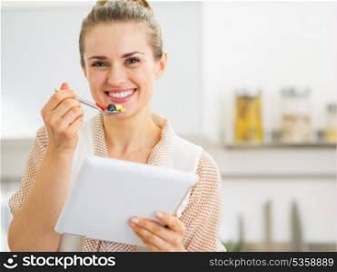 Happy young housewife with tablet pc eating fruits salad