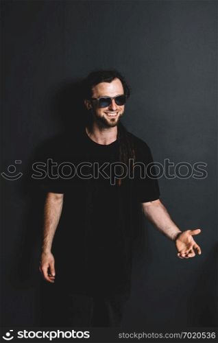 Happy young in sunglasses standing on a black background. Casual portrait.. Happy young in sunglasses standing on a black background.