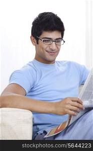 Happy young Indian man reading newspaper at home