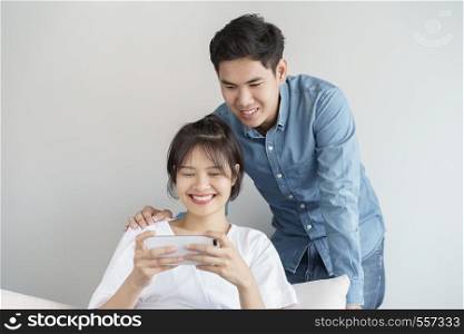 Happy young love asian couple sitting on a couch at home, looking at mobile phone, Young asian people are using smartphone