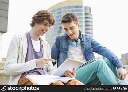 Happy young male college students using digital tablet against building