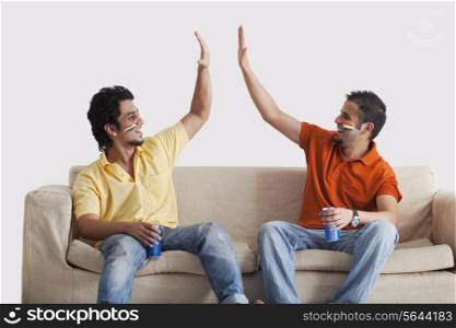 Happy young male friends in casuals giving a high-five to each other while holding tin cans