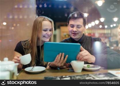 Happy young man and woman drinking coffee while looking on tablet