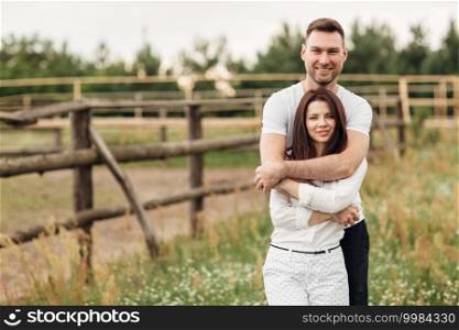 happy young man and woman having fun outdoors on a warm summer day. couple is hugging in the park near wooden fence.. happy young man and woman having fun outdoors on a warm summer day. couple is hugging in the park near wooden fence