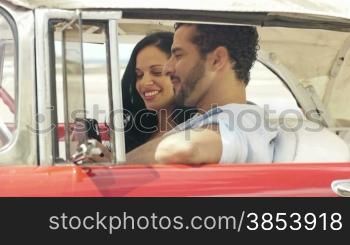 Happy young man and woman smiling while taking snapshot with cell phone camera from red vintage convertible car