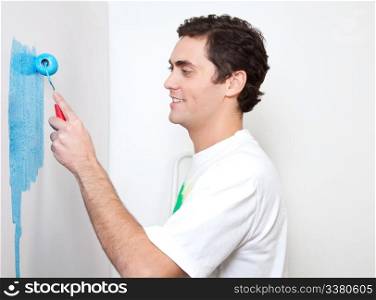 Happy young man applying sky blue color to the wall