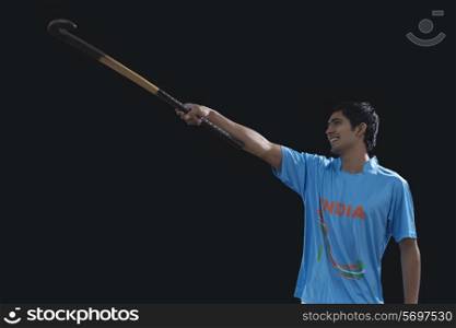 Happy young man celebrating victory by raising hockey stick isolated over black background