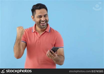 Happy young man cheering with raising his fist while using Smartphone 