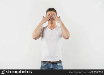 happy young man covering his eyes with two hands against white background
