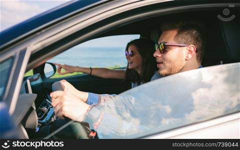 Happy young man driving a car accompanied by his girlfriend. Young man driving a car with his girlfriend