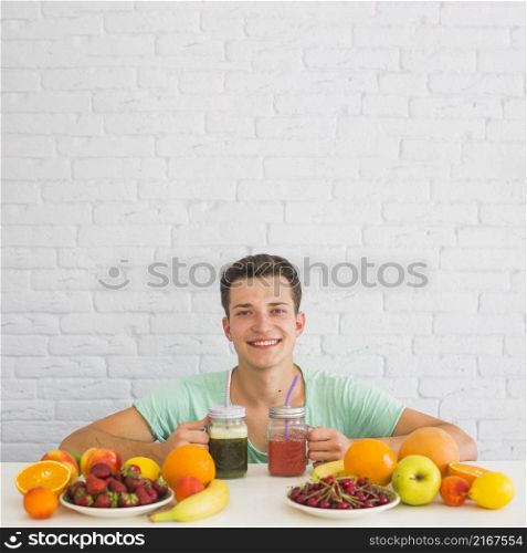 happy young man holding smoothies with colorful fresh organic fruits desk