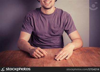 Happy young man in a purple top is sitting at a table