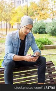 Happy young man in casual wear holding mobile phone while sitting outdoors