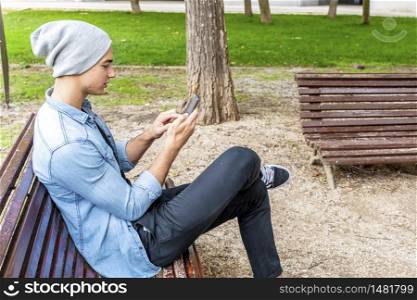 Happy young man in casual wear holding mobile phone while sitting outdoors