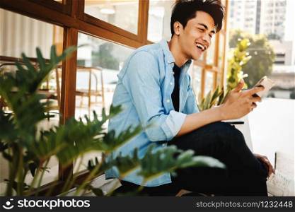 Happy Young Man in Casual wear Using Mobile Phone while Sitting in front of the Cafe. Lifestyle of Modern People