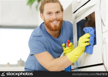 happy young man in overall cleaning oven