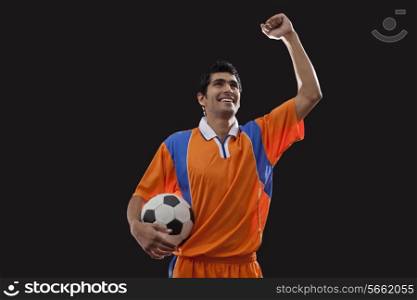 Happy young man in sports clothing celebrates victory while holding ball over black background