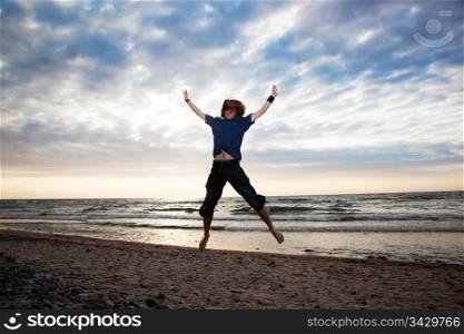 Happy young man jumping on the beach during sunset