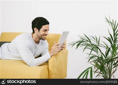 happy young man laying sofa with tablet