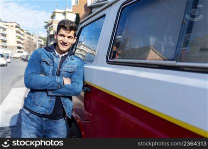 Happy young man leaning at the retro mini van outdoor