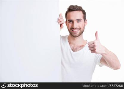 Happy young man look out from blank banner with thumb up - isolated on white.