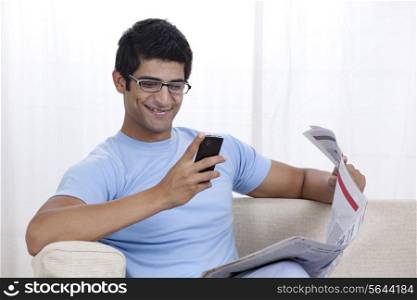 Happy young man looking at mobile phone while sitting on sofa