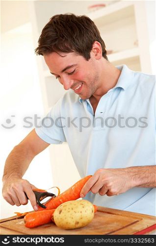 Happy young man peeling vegetable in kitchen