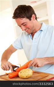 Happy young man peeling vegetable in kitchen