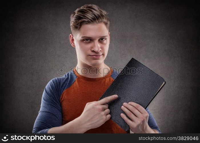 Happy young man pointing a big book with leather covers