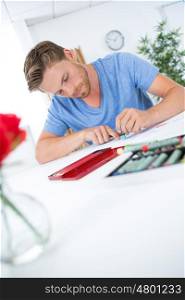 happy young man sitting at desk at home happily drawing