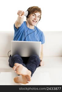 Happy young man sitting on the couch with arms up and a laptop over the legs