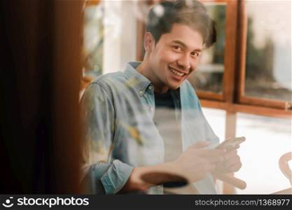 Happy Young Man Smiling and Looking at Camera through Glass Window while Sitting in Cafe