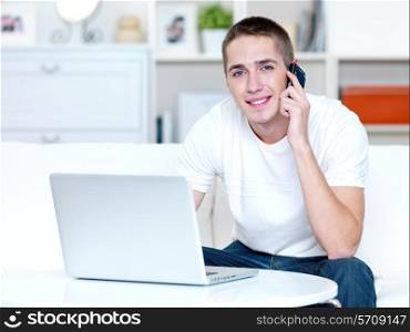 happy young man speaks on the phone and works on the laptop at home