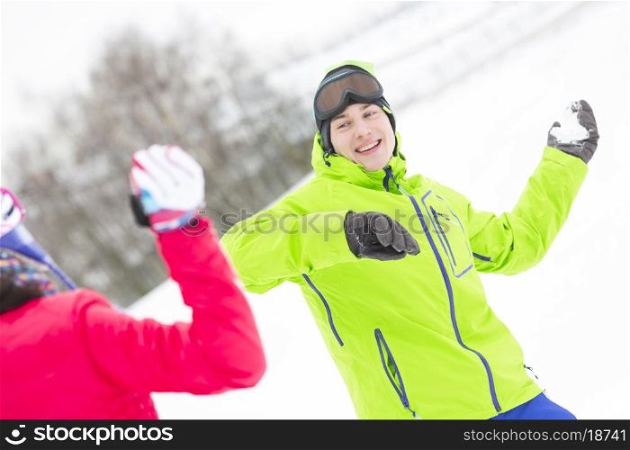 Happy young man throwing snowball towards woman