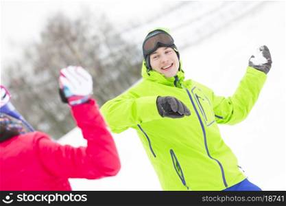 Happy young man throwing snowball towards woman