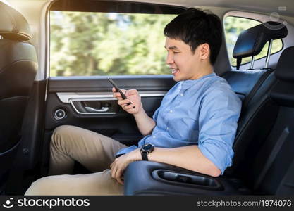 happy young man using a smartphone while sitting in the back seat of car