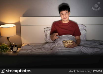 happy young man watching TV on a bed at night