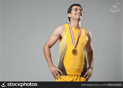 Happy young man wearing gold medal with hands on hip isolated over gray background