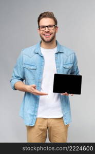 Happy young man wearing jeans shirt standing and holding tablet pc pad over studio grey background.. Happy young man wearing jeans shirt standing and holding tablet pc pad over studio grey background