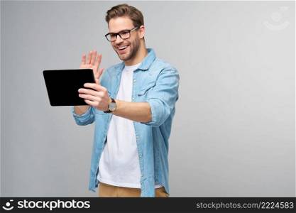 Happy young man wearing jeans shirt standing and using tablet over studio grey background.. Happy young man wearing jeans shirt standing and using tablet over studio grey background