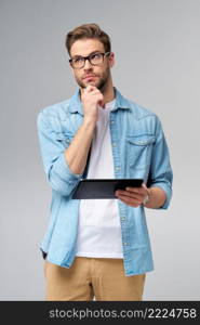 Happy young man wearing jeans shirt standing and using tablet over studio grey background.. Happy young man wearing jeans shirt standing and using tablet over studio grey background