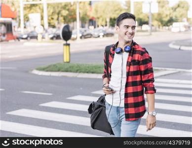 happy young man with cellphone crossing street